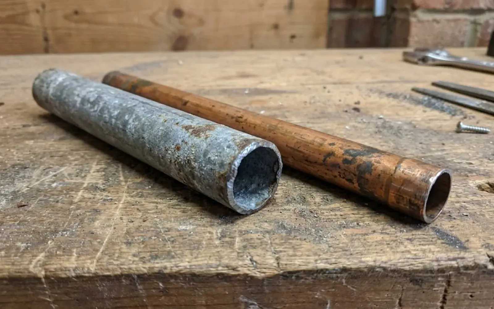 Galvanized steel pipe and copper pipe lying side by side on a workbench