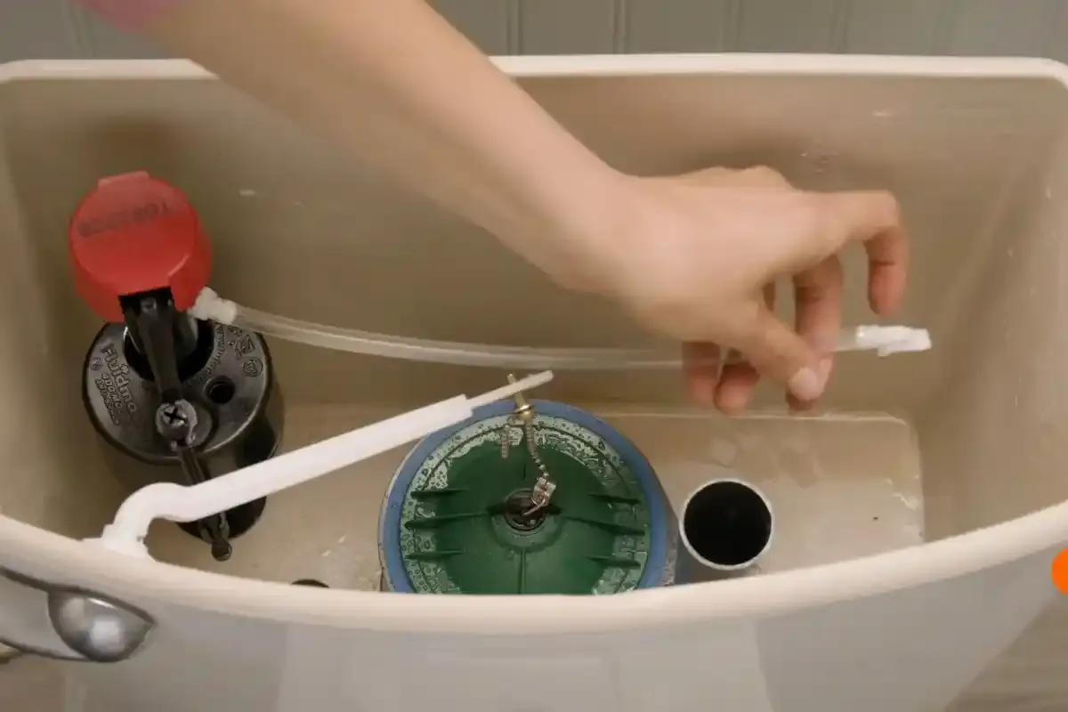 Hand adjusting the flapper and fill valve inside a toilet tank