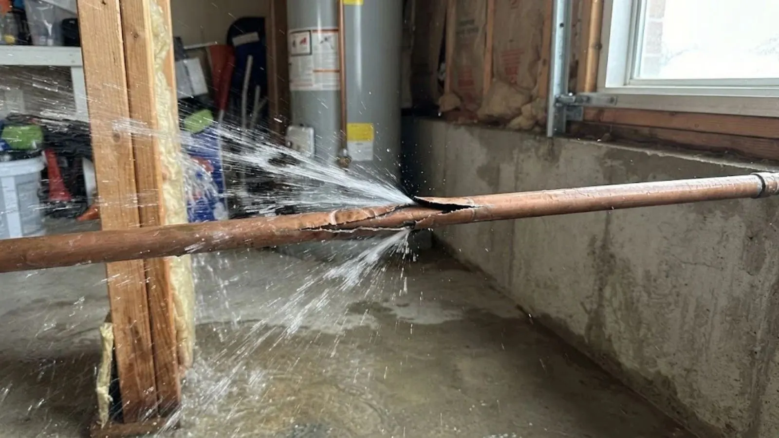 Burst copper water pipe spraying water across a garage wall