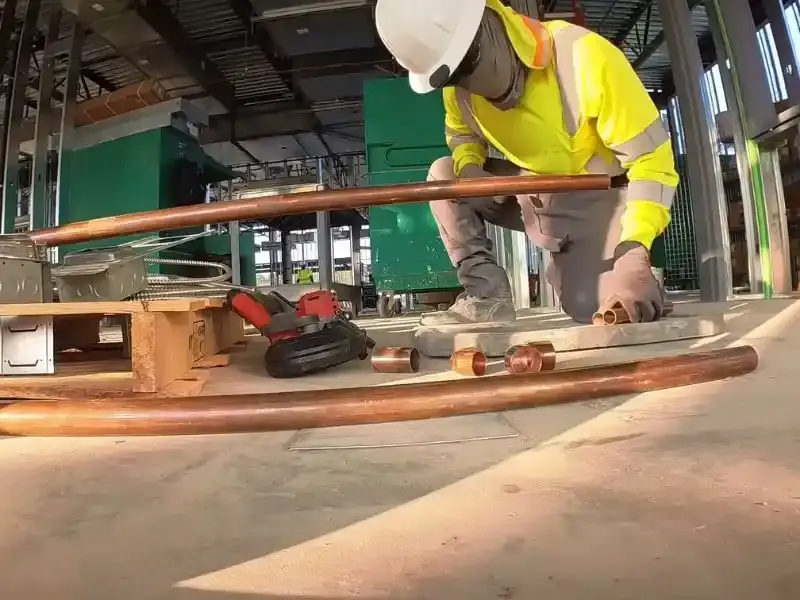Worker in a high-visibility vest handling copper pipe in a large industrial building