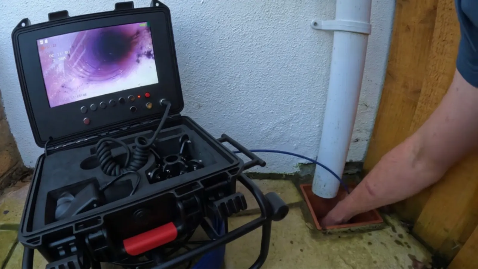 Sewer inspection camera monitor in a hard case next to a cleanout pipe